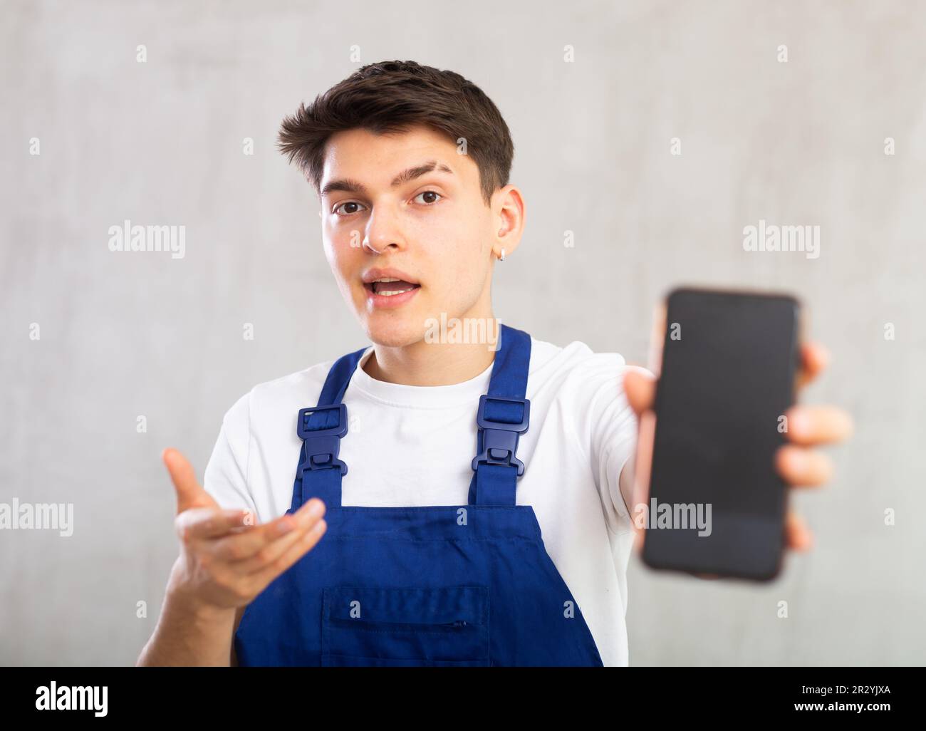 Man in blue jumpsuit shows dark empty mobile phone screen and points at device with his hand Stock Photo