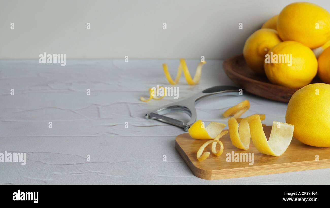 Wooden board, lemons, peeler and fresh rind on white textured table