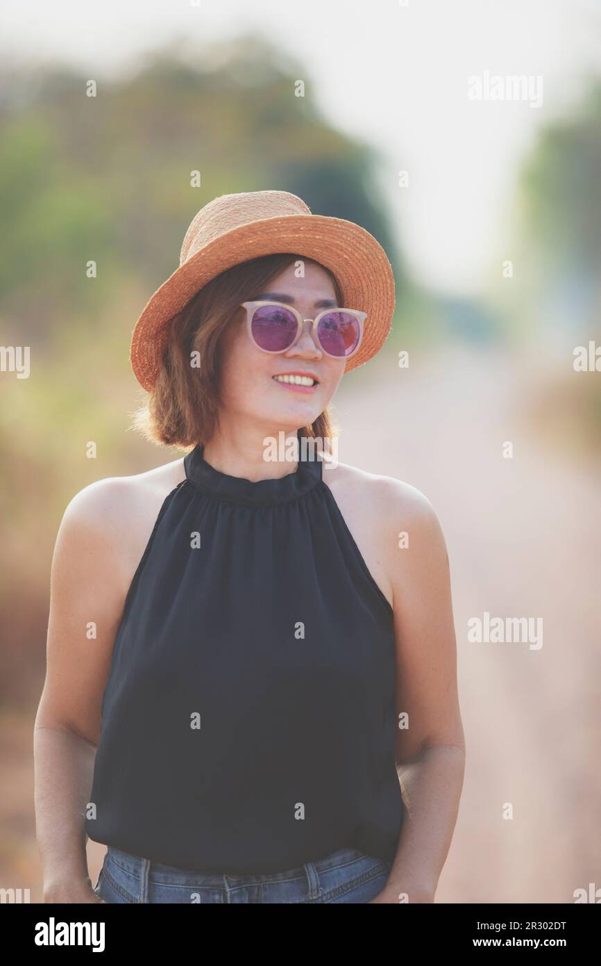 beautiful asian woman wearing straw hat toothy smiling with happiness standing outdoor against beautiful morning light Stock Photo