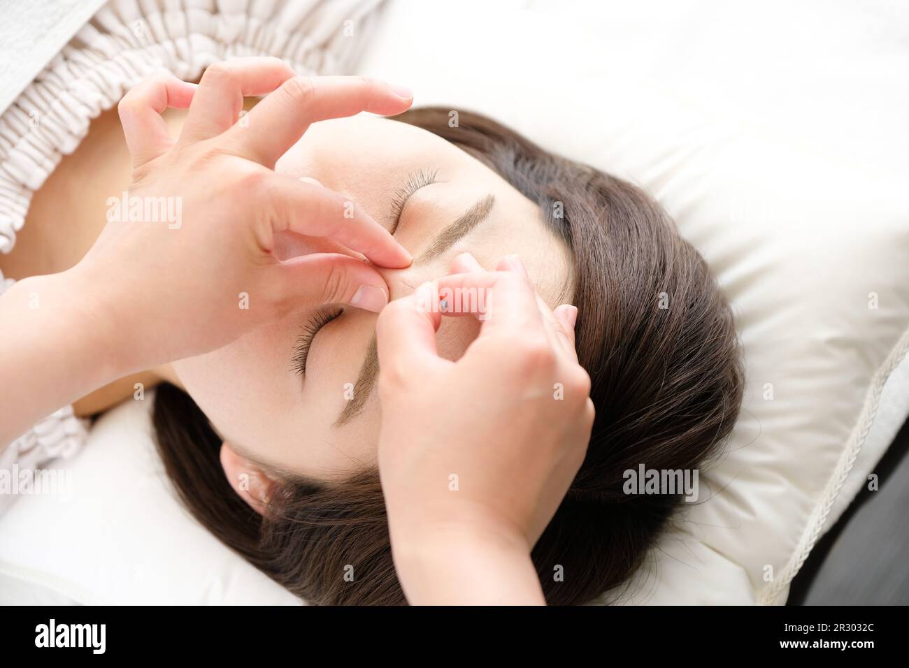 Close-up of a woman and her practitioner's hands being given acupuncture needles on her face in an acupuncture clinic. Stock Photo