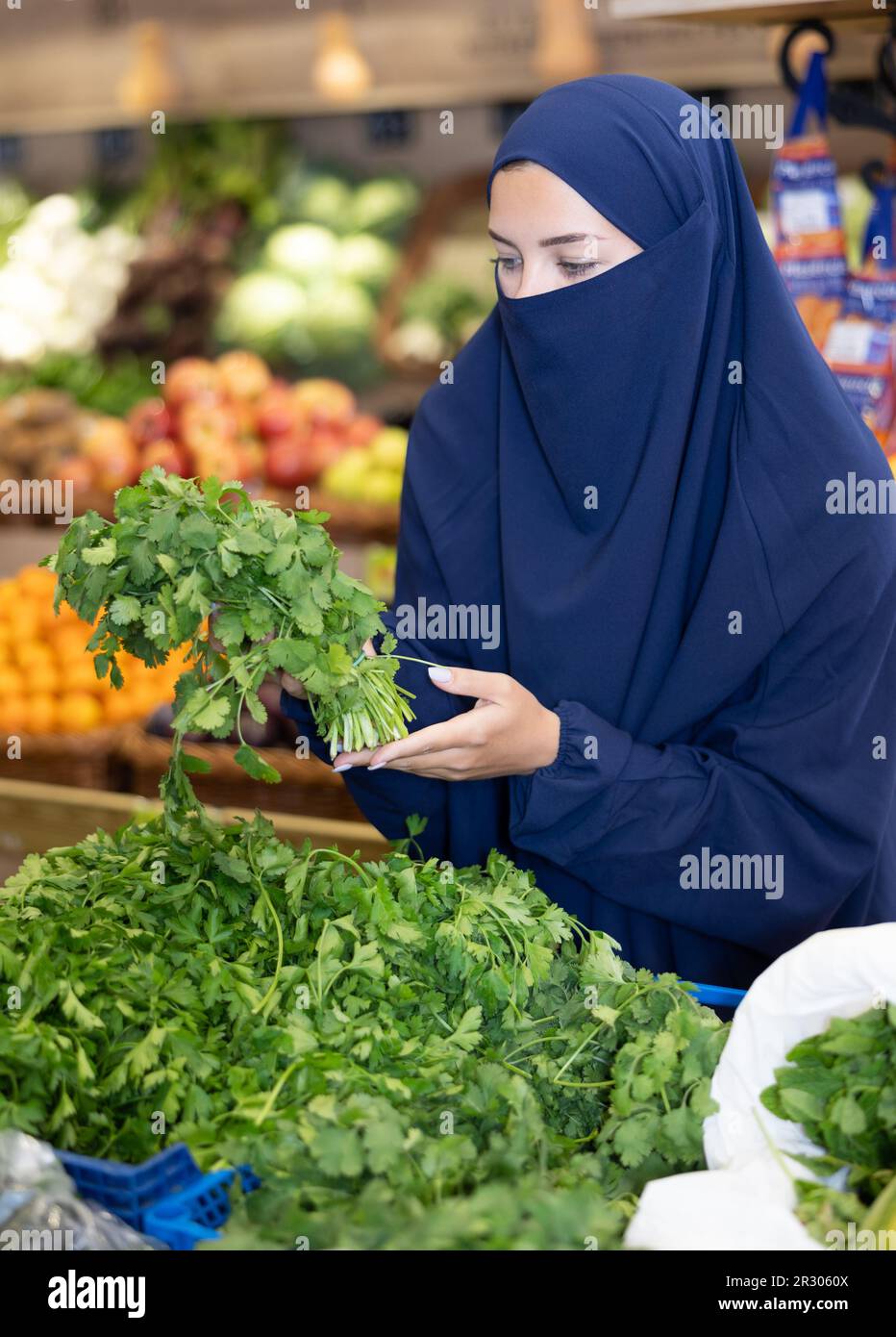 Girl in veil carefully chooses fresh parsley in supermarket Stock Photo