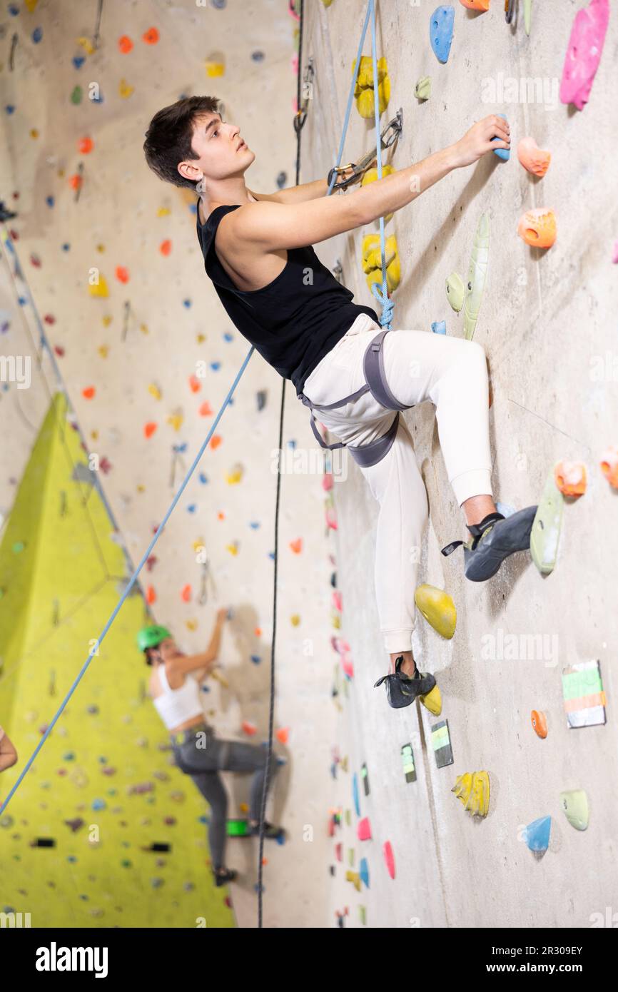 Determined young man doing his best at climbing artificial wall Stock Photo