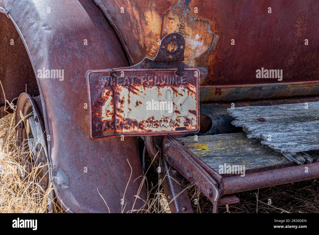 An old, rusty Saskatchewan license plate attached to an abandoned