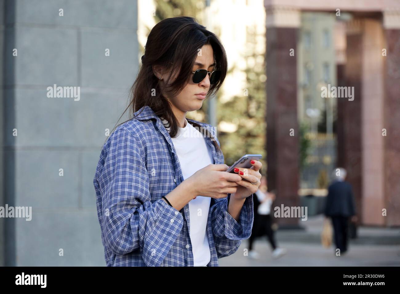 Girl in sunglasses standing on a street with smartphone. Using mobile phone in spring city Stock Photo