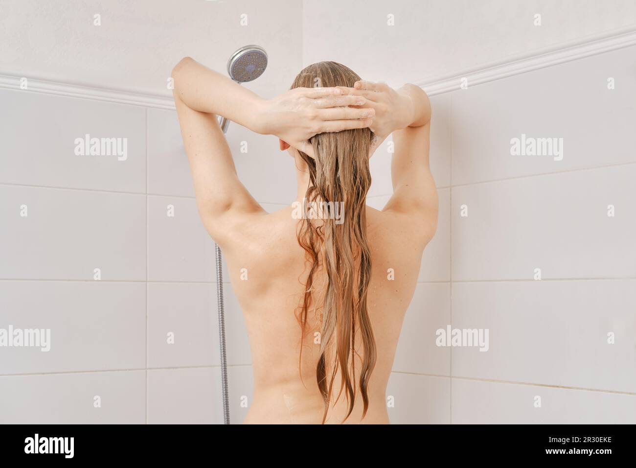 Back view of young woman with healthy skin washes her hair with shampoo  in bathroom Stock Photo