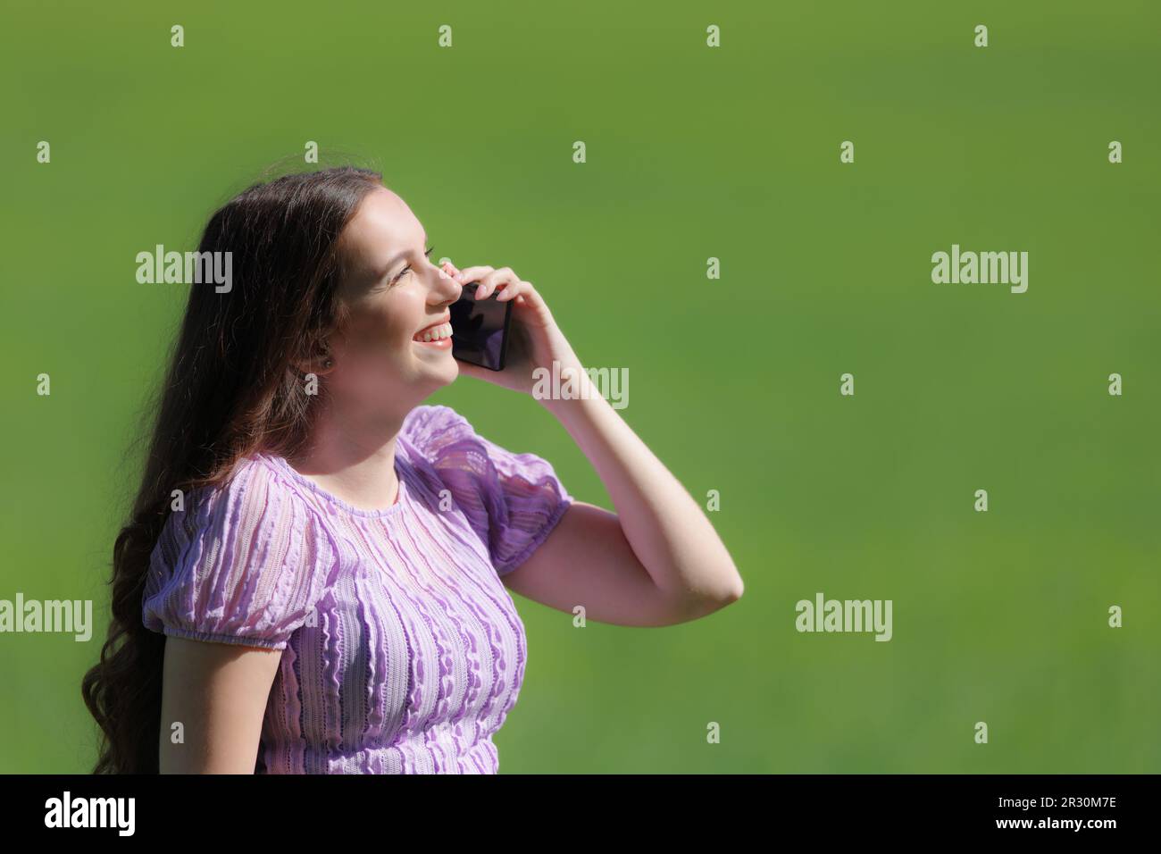 Profile of a happy woman talking on phone on green field Stock Photo