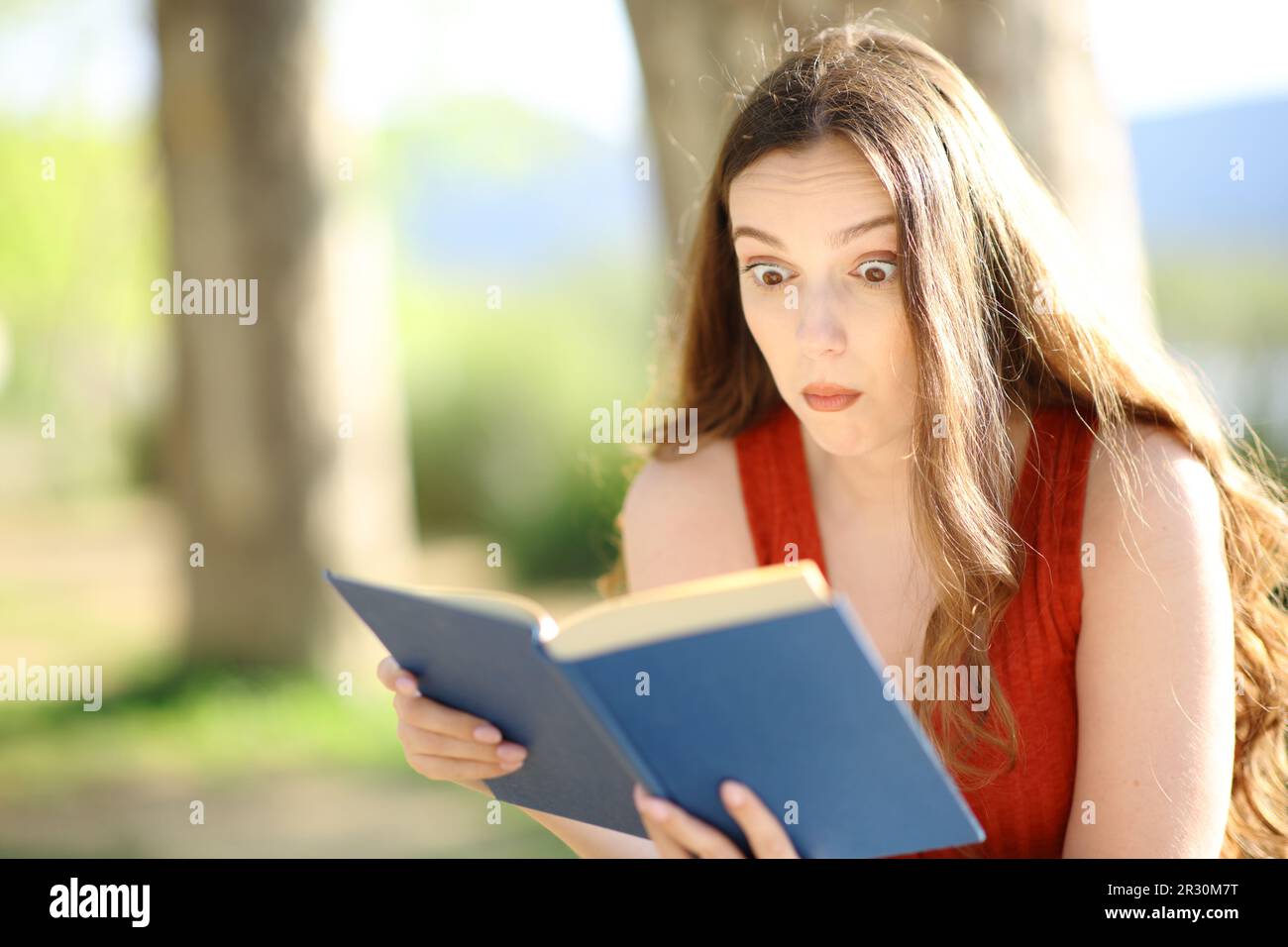 Perplexed reader reading a paper book outdoors sitting in nature Stock Photo