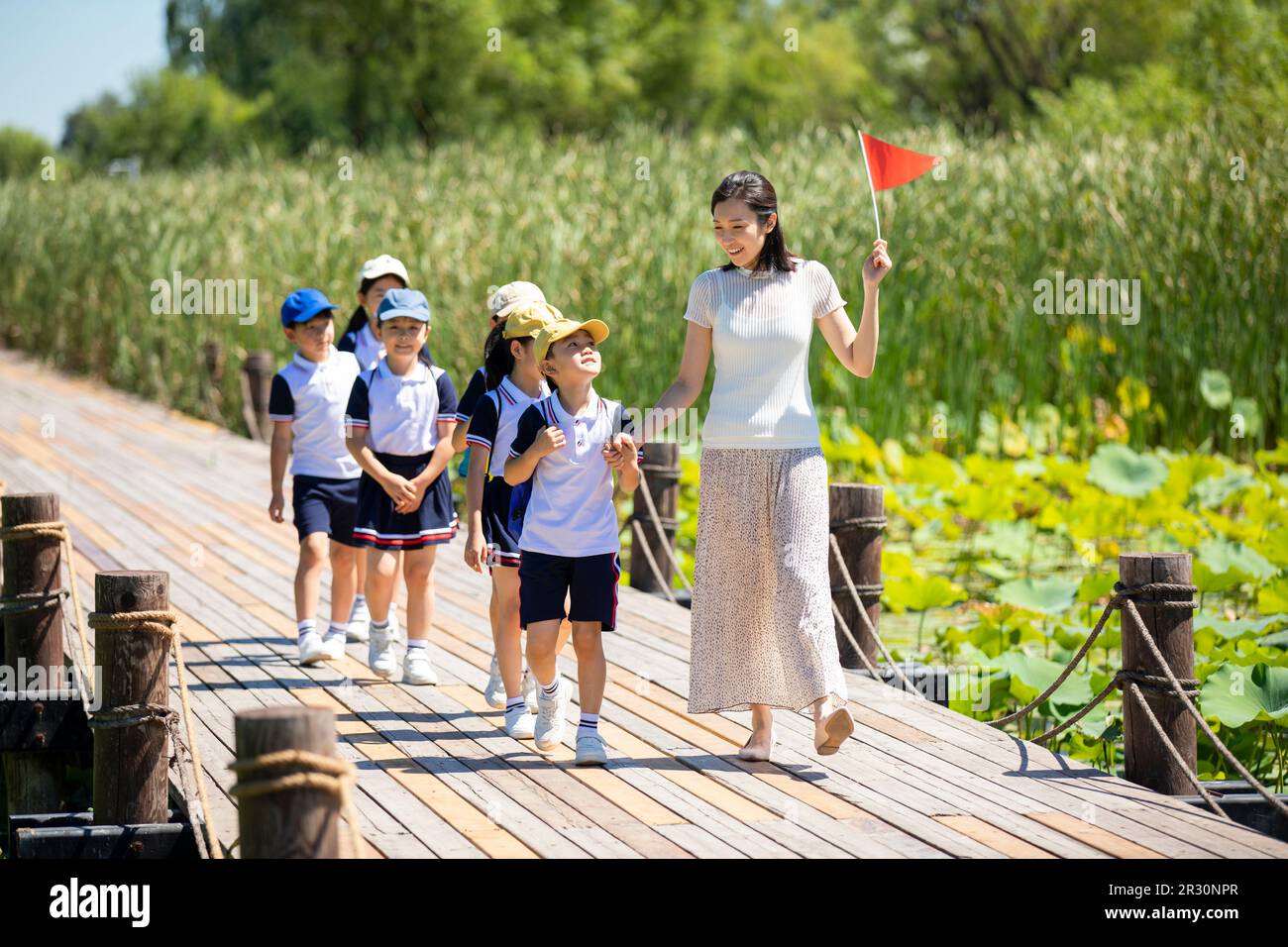 Cheerful Chinese school children walking in park with their teacher ...