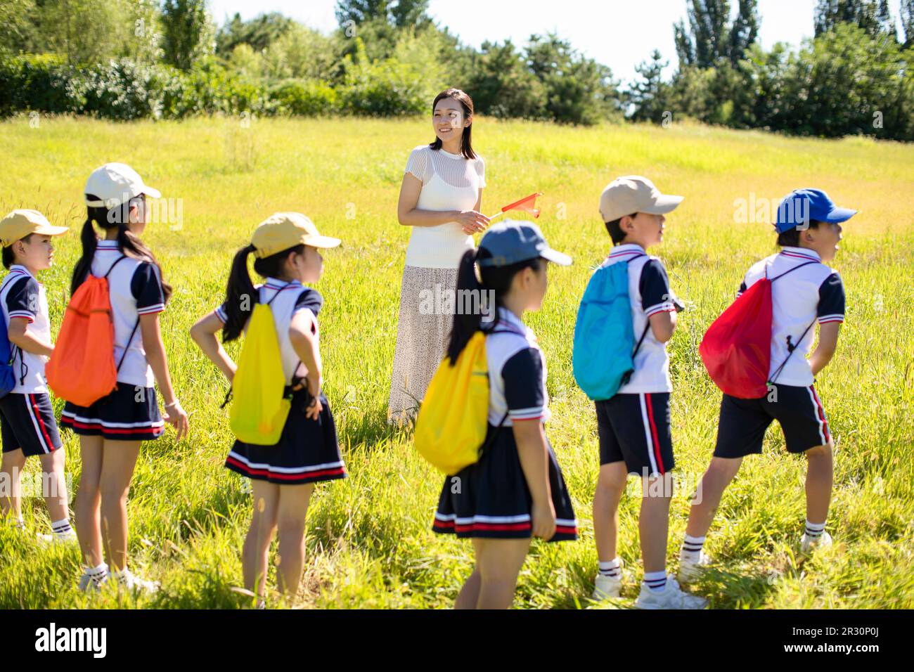 Cheerful Chinese school children relaxing in park with their teacher ...