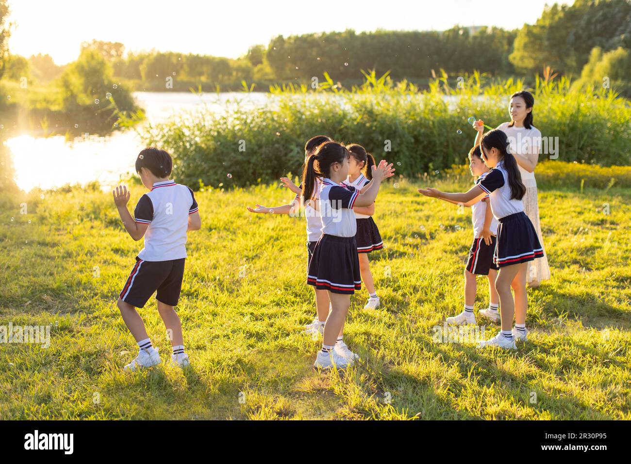 Cheerful Chinese school children and their teacher blowing bubbles on ...