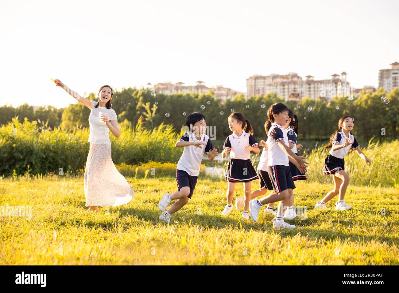 Cheerful Chinese school children and their teacher blowing bubbles on ...