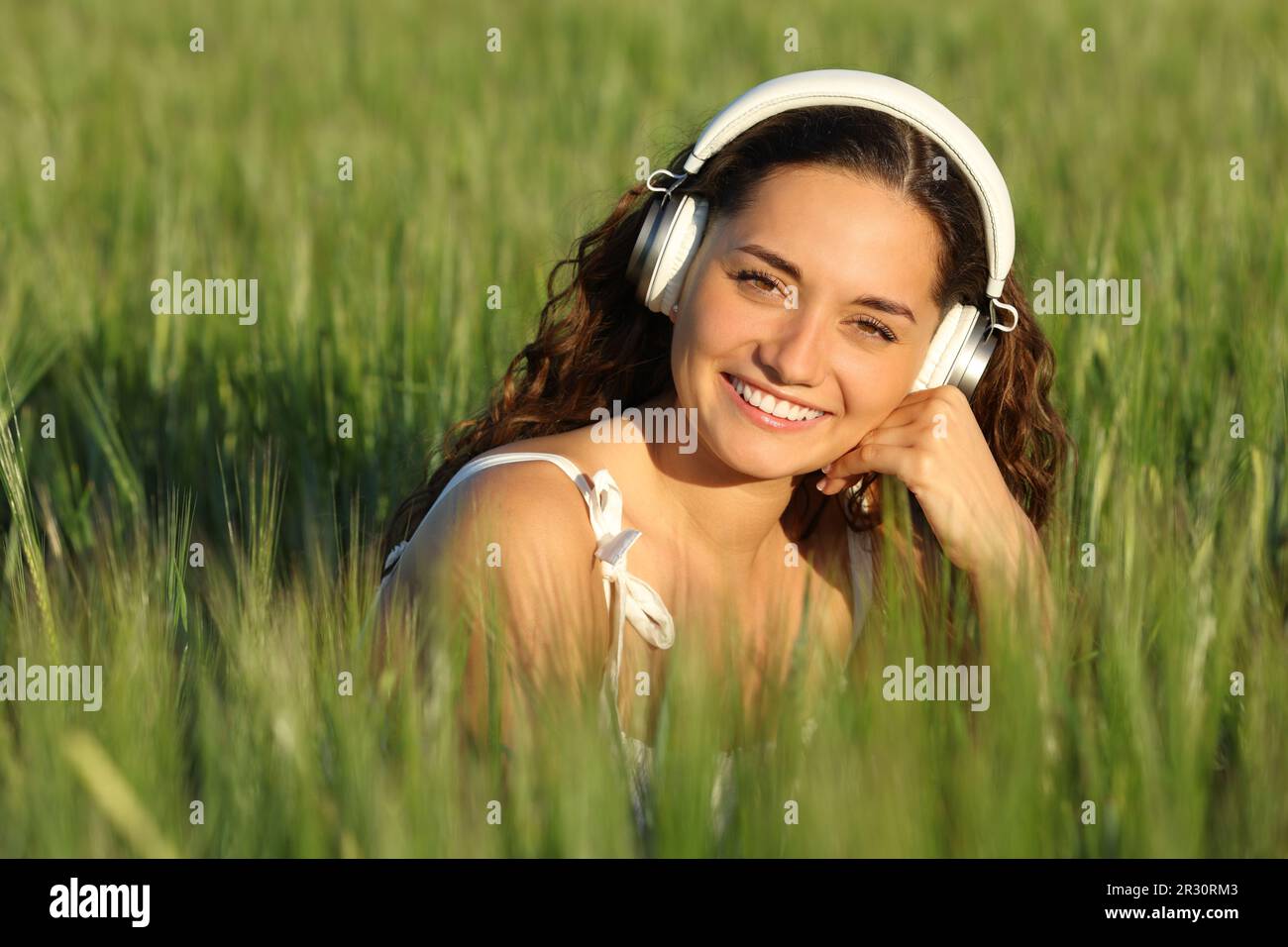 Happy woman in a green field looks at you with heaphone Stock Photo
