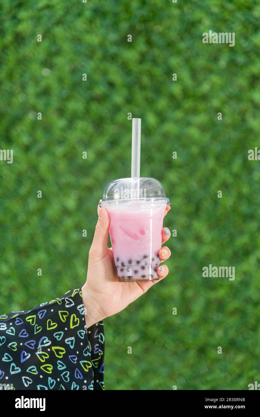 Woman holding bubble tea with lemonade in front of green grass wall Stock Photo