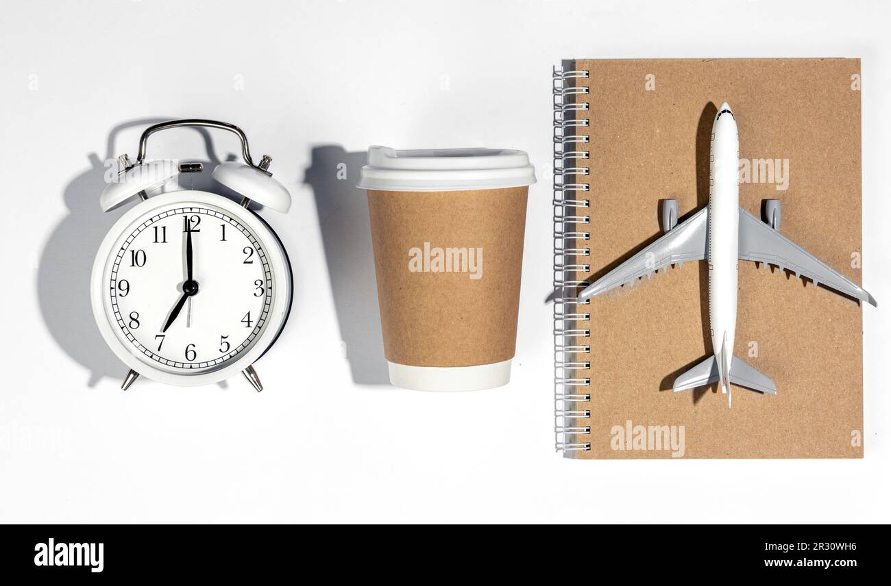 Alarm clock, paper cup, airplane model and notebook on white background ...