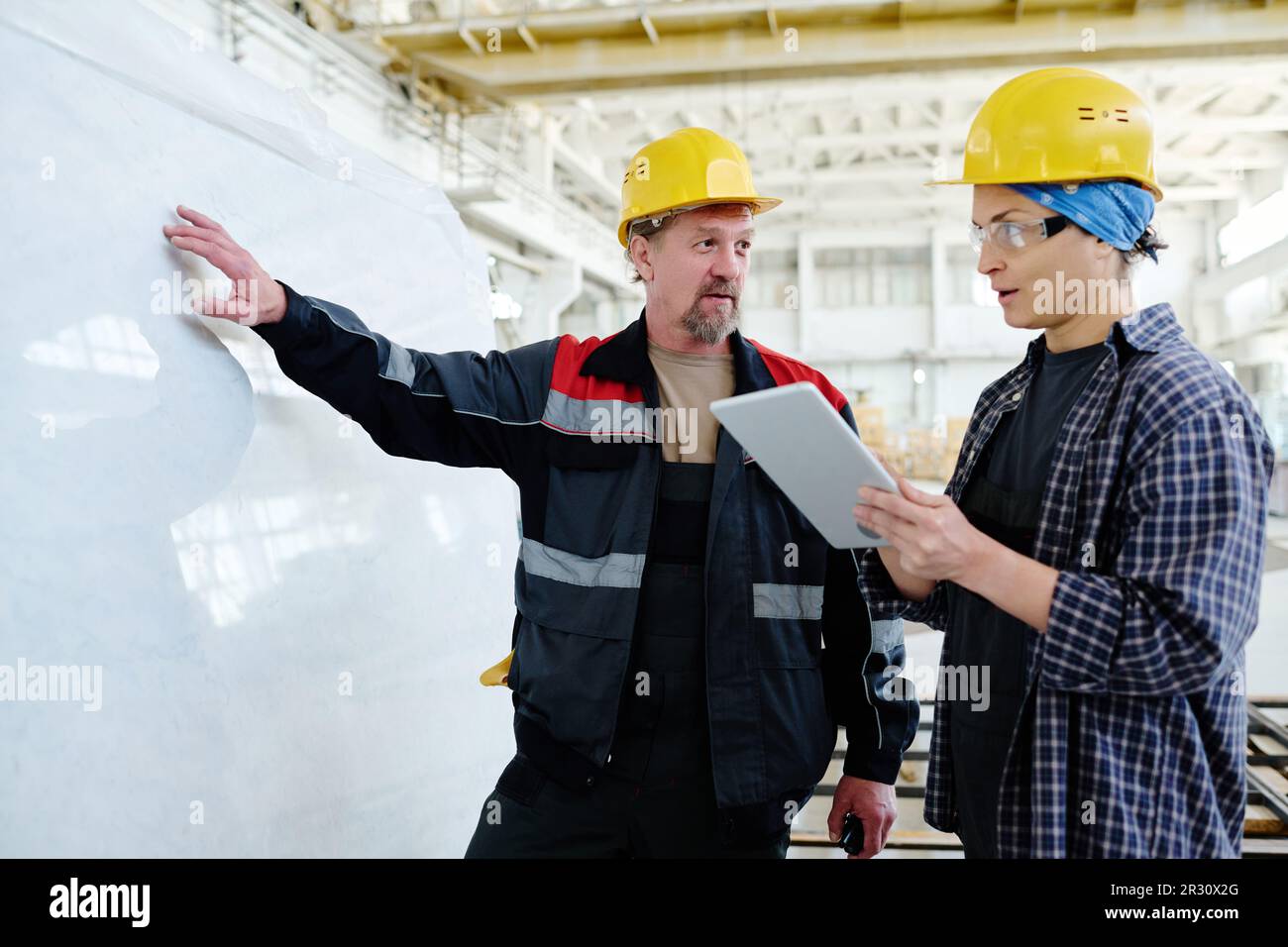 Two colleagues using digital tablet while discussing the material for production standing in workshop Stock Photo