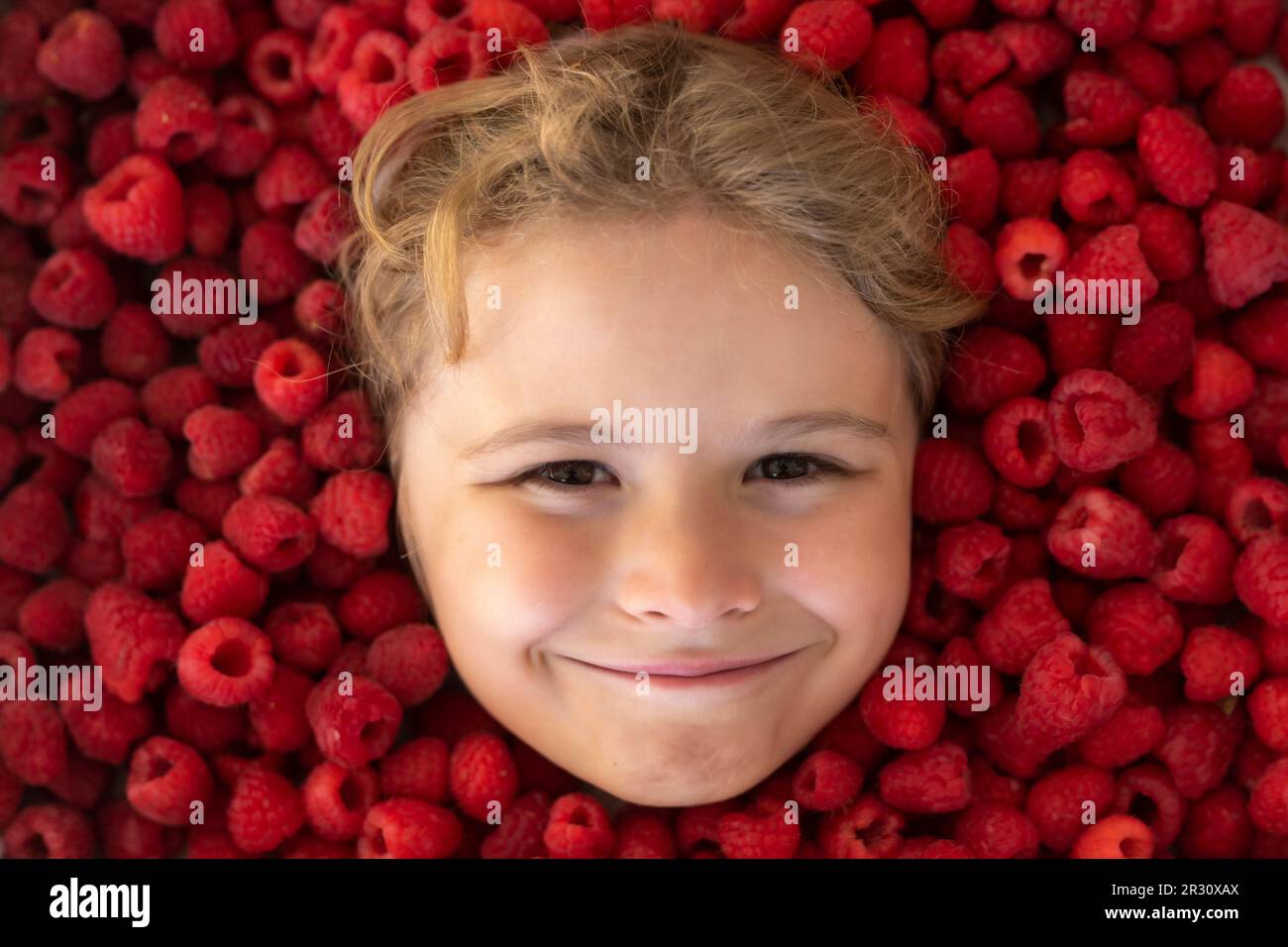 Happy little child face with raspberry. Child picking raspberry. Kids