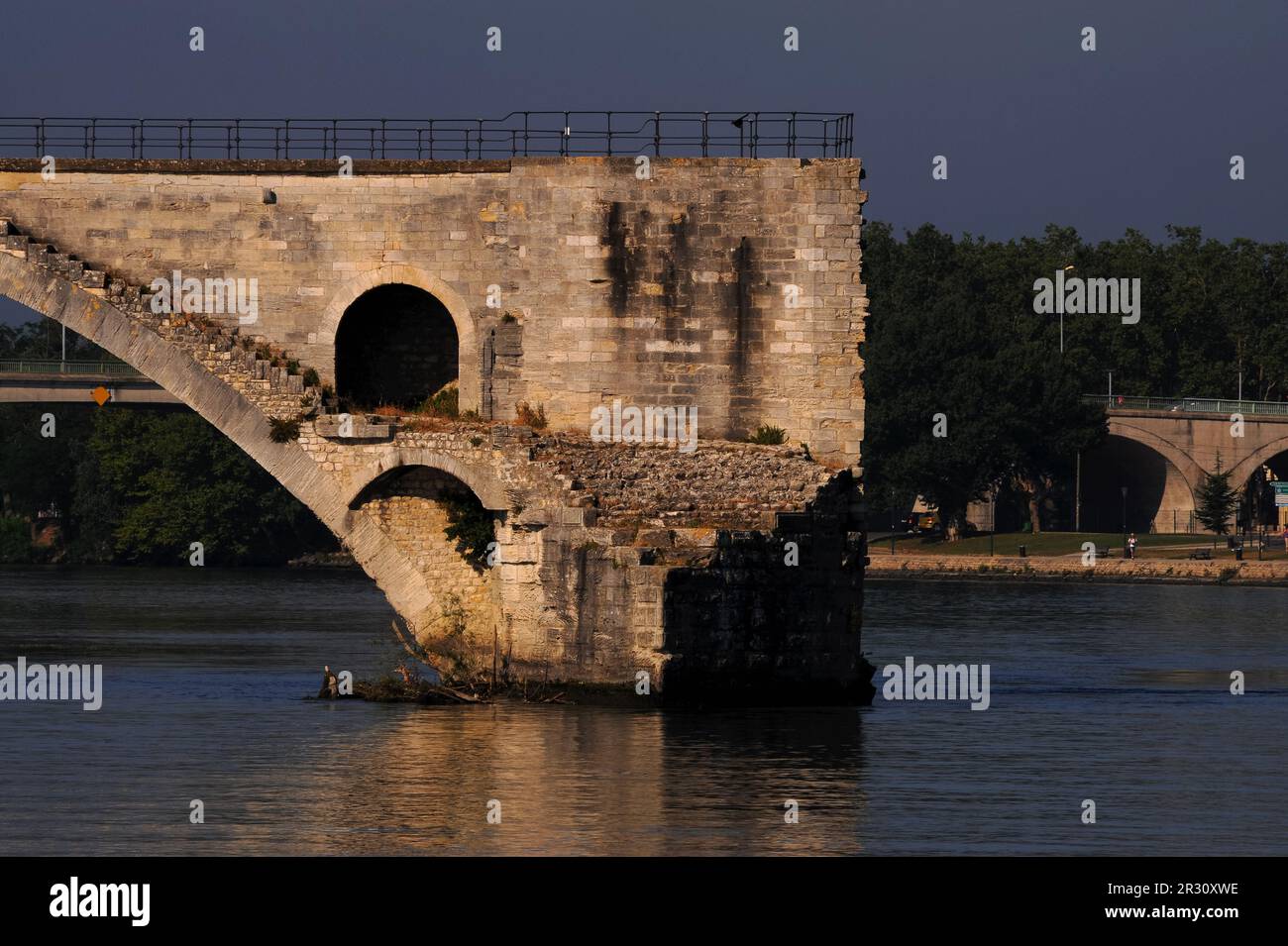 The ruined Pont d’Avignon or Pont Saint-Bénézet, a medieval bridge over the River Rhône where only four arches out of an original 22 have survived, the rest swept away by floods or destroyed in war.  At Avignon, capital of the Vaucluse department in the Provence-Alpes-Côte-d’Azur region of France.  This photograph was shot on an early July morning, between 7am and 8am. Stock Photo