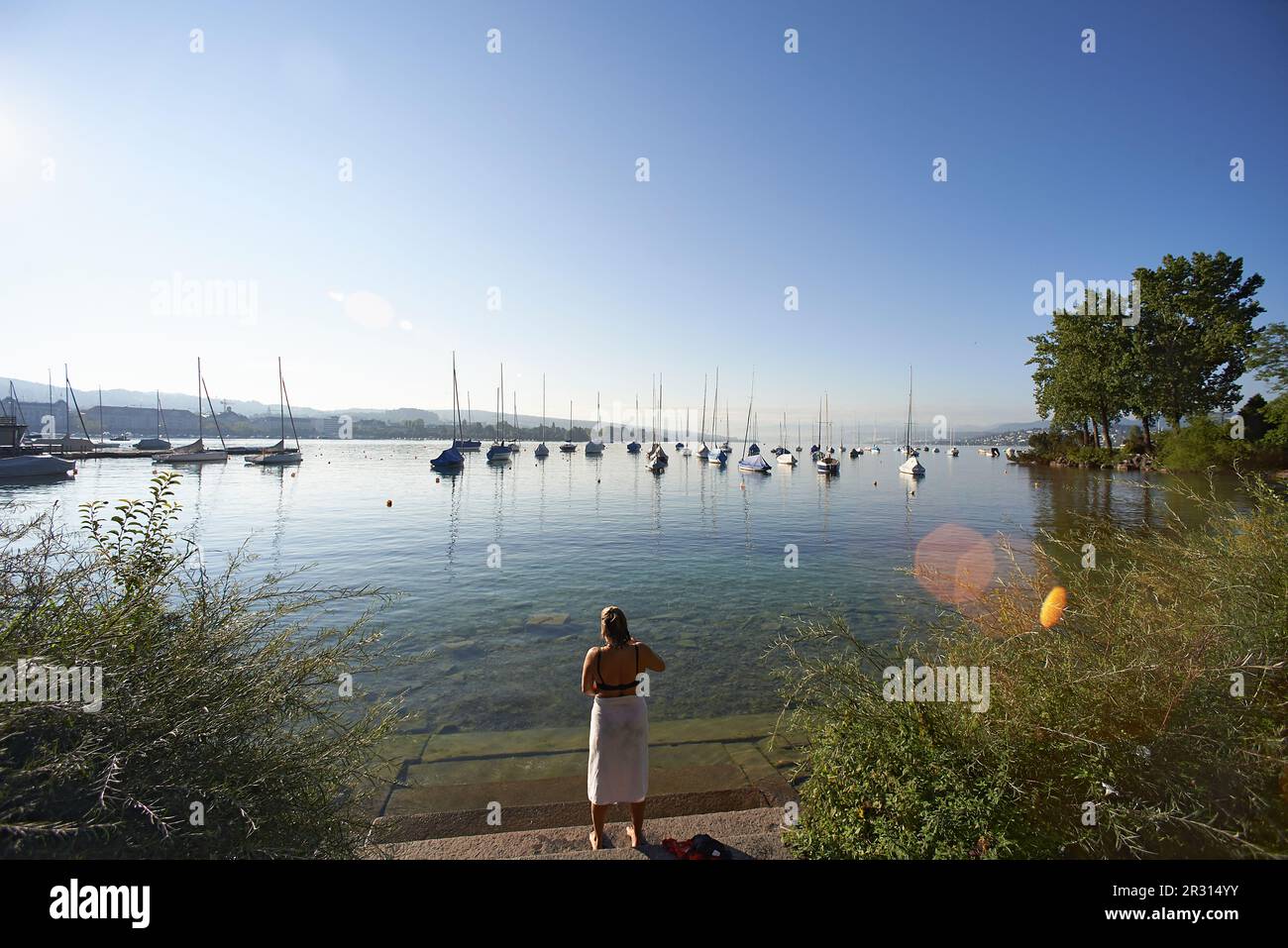 Elderly Woman Wrapped In A Towel Standing Along Shore Of Lake Zurich 