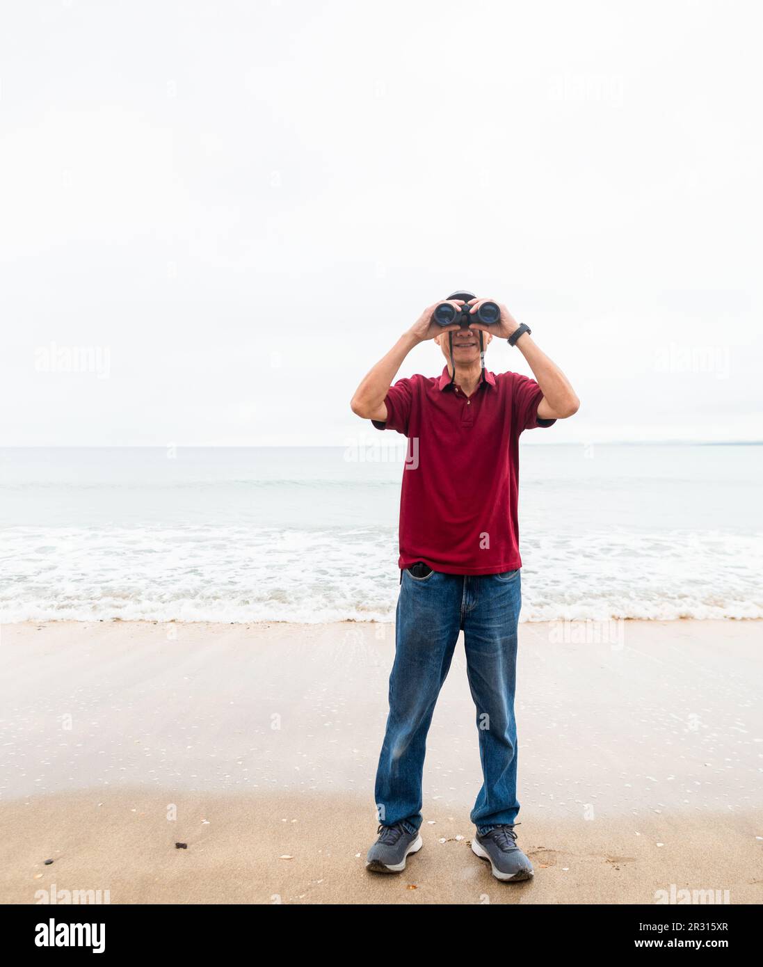 Man smiling while looking at the camera through a pair of binoculars at beach. Vertical shot. Stock Photo