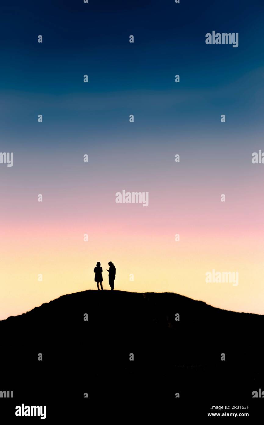 The silhouette of two people standing on an ancient bronze age bowl barrow on Barrowfields in Newquay in Cornwall in the UK. Stock Photo