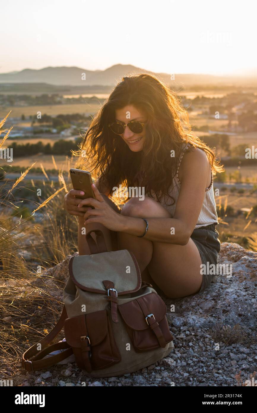 Young woman is watching her smartphone on top of a mountain Stock Photo