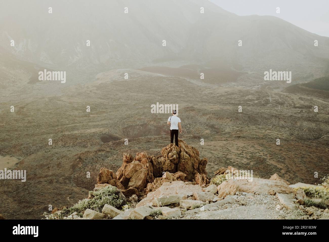 Pulled back view of man standing on rock with lava landscape in back ...
