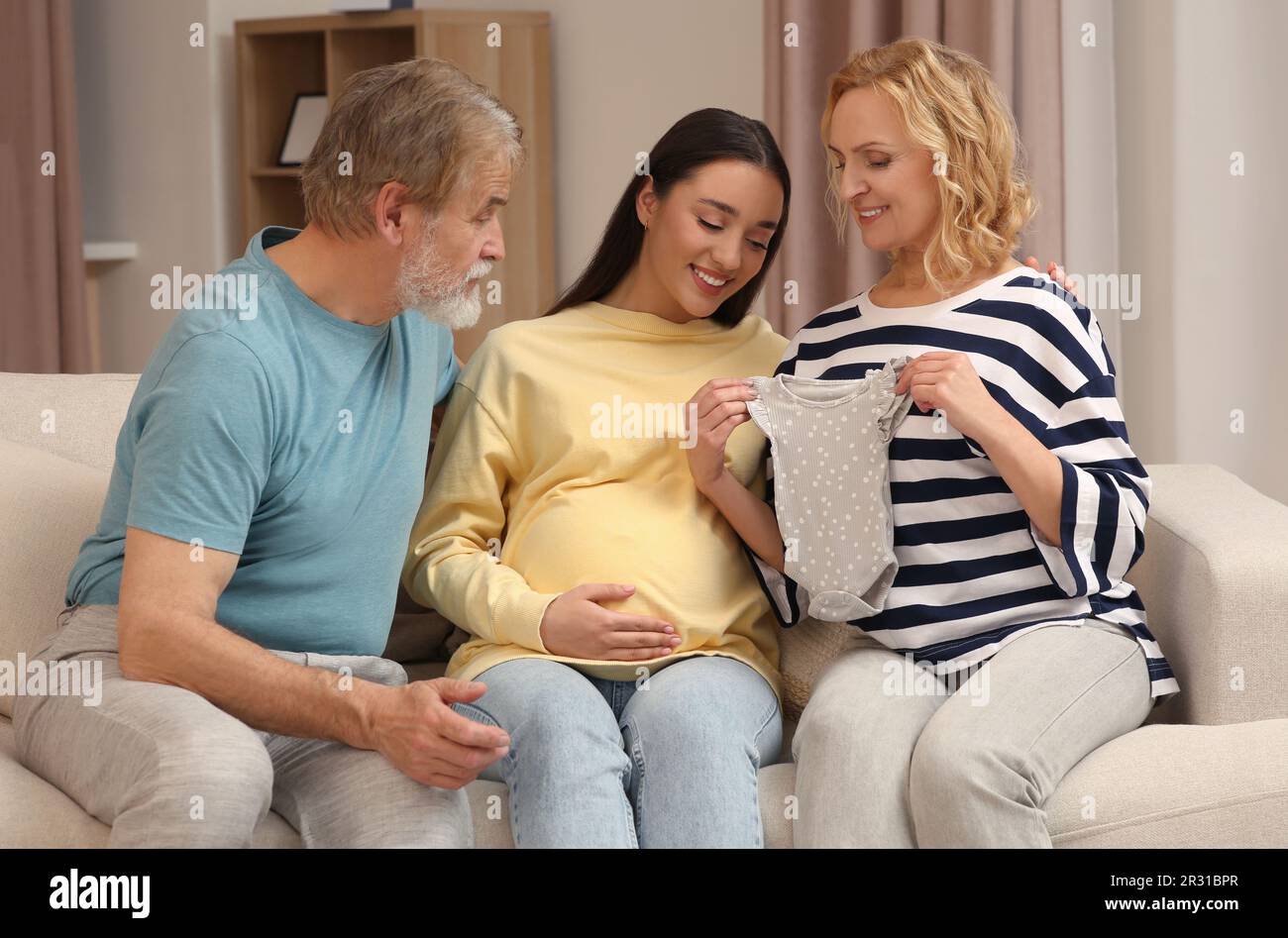Happy pregnant woman spending time with her parents at home. Grandparents' reaction to future grandson Stock Photo