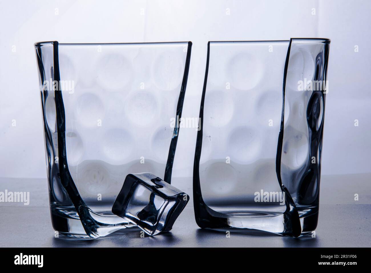 Glass broken in two halves with an ice cube. Photographed on white