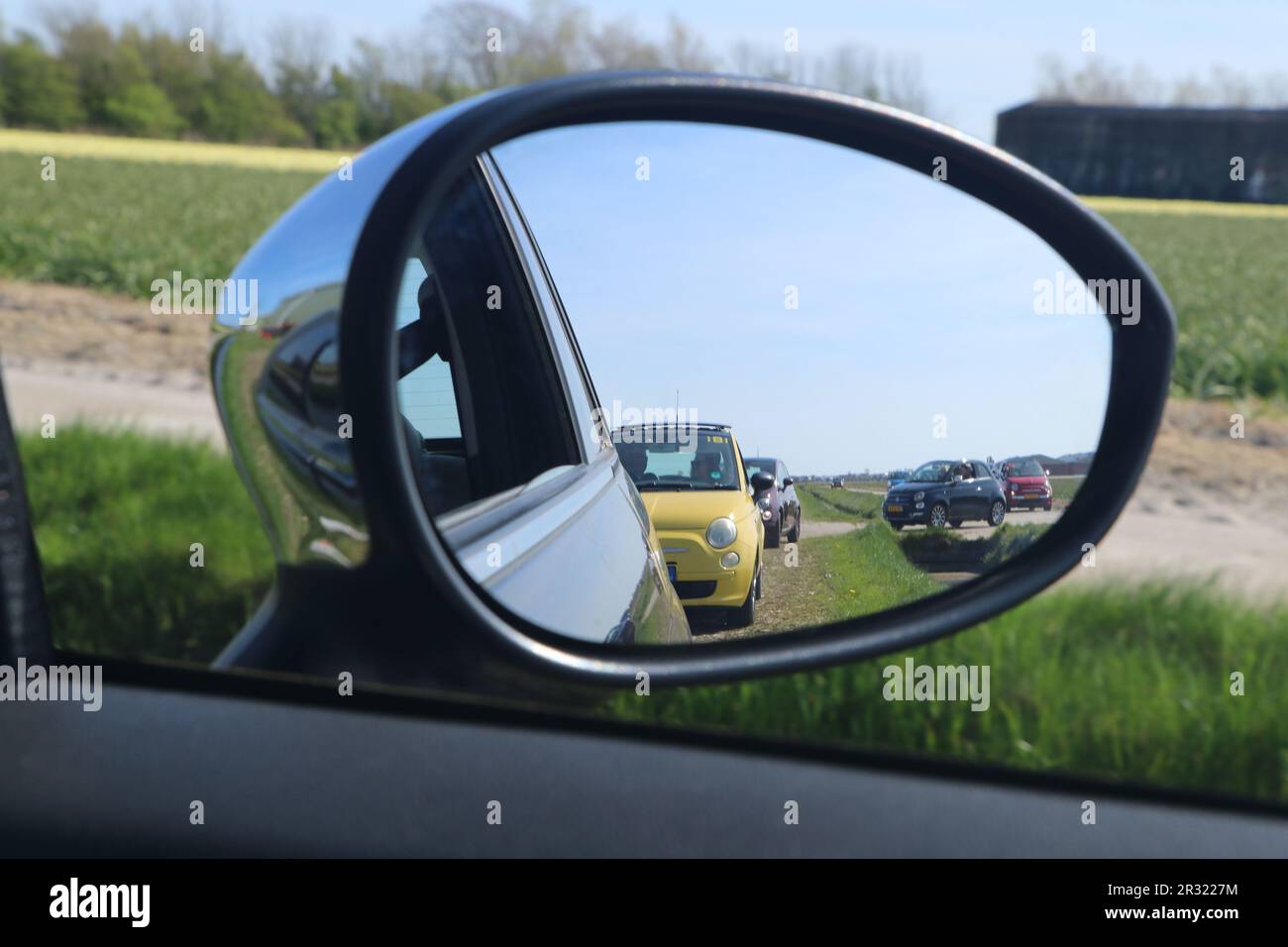 side view mirror reflecting several Fiat 500 cars in dutch landscape in Julianadorp, the Netherlands - April 30 2023 Stock Photo