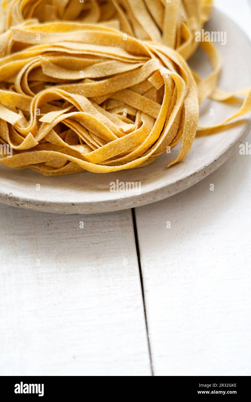 Uncooked whole wheat tagliatelle on a white wooden background, Italy, Europe Stock Photo