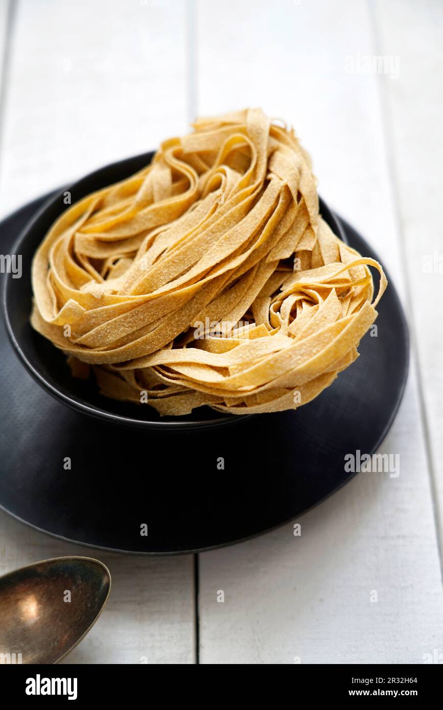 Uncooked whole wheat tagliatelle on a white wooden background, Italy, Europe Stock Photo