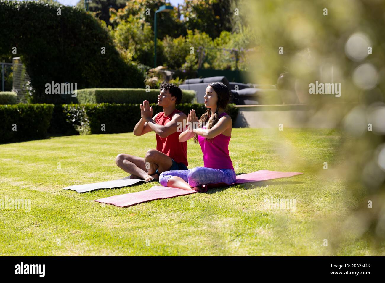 Happy diverse fit couple practicing yoga meditation sitting in sunny garden Stock Photo