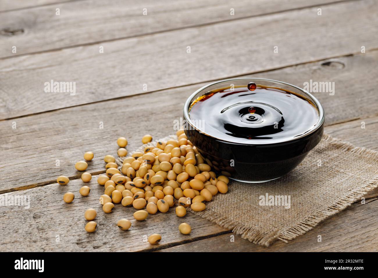 soy sauce in glass bowl with falling drops and dry soybeans on table Stock Photo
