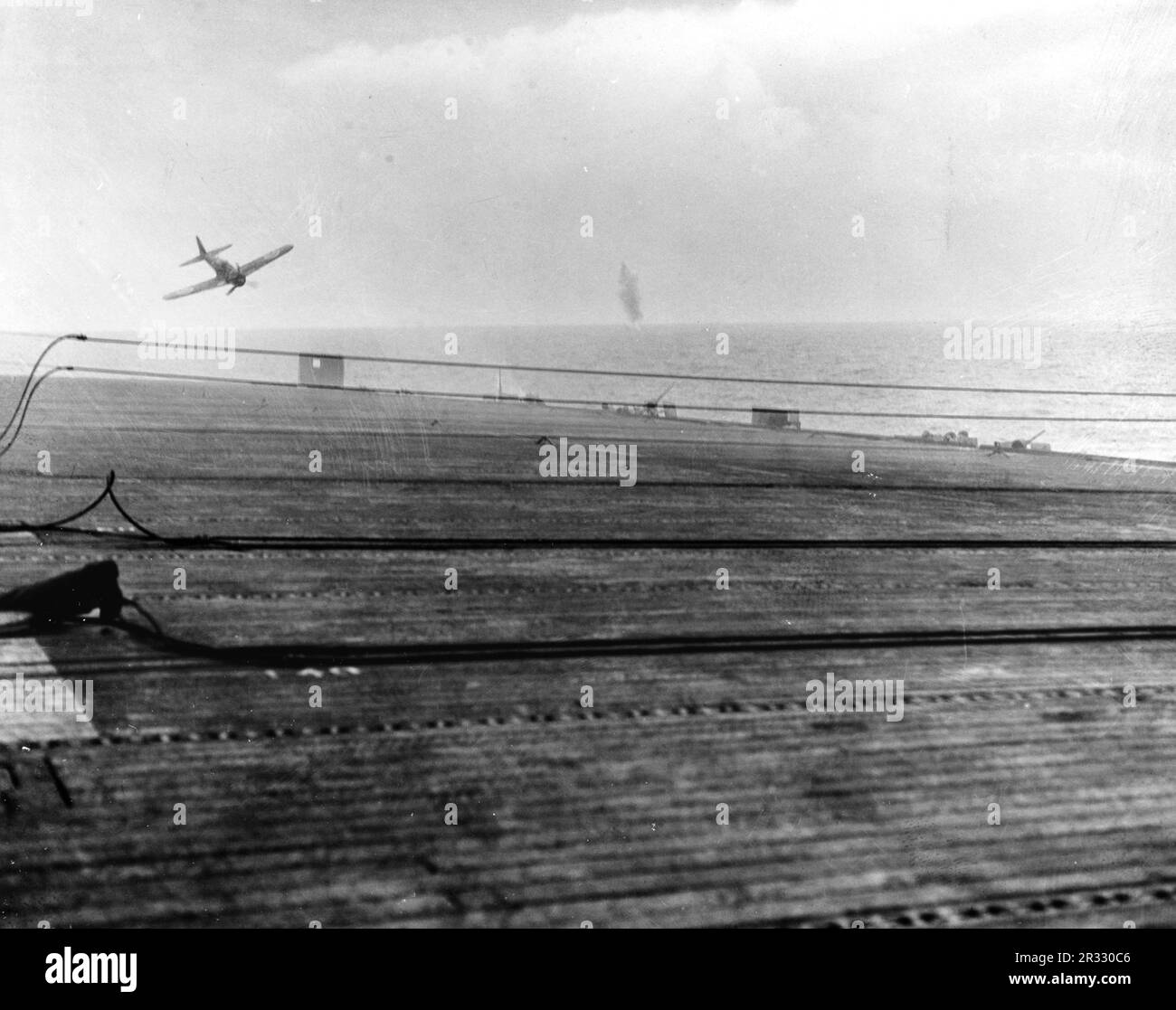 A Japanese kamikaze pilot in a Mitsubishi A6M5 Model 52 ('Zero') crash dives on the U.S. Navy escort carrier USS White Plains (CVE-66) on 25 October 1944. The aircraft missed the flight deck and impacted the water just off the port quarter of the ship. When Japan was facing defeat in late 1944 it chose to destroy US ships with suicide bombings, known as Kamikaze.These attacks were a potent physical and psychological weapon and sunk a total of 47 ships at a cost of more than 3000 pilots and planes. By late 1944 the US Navy was large enough that the losses were insignificant and they did not alt Stock Photo