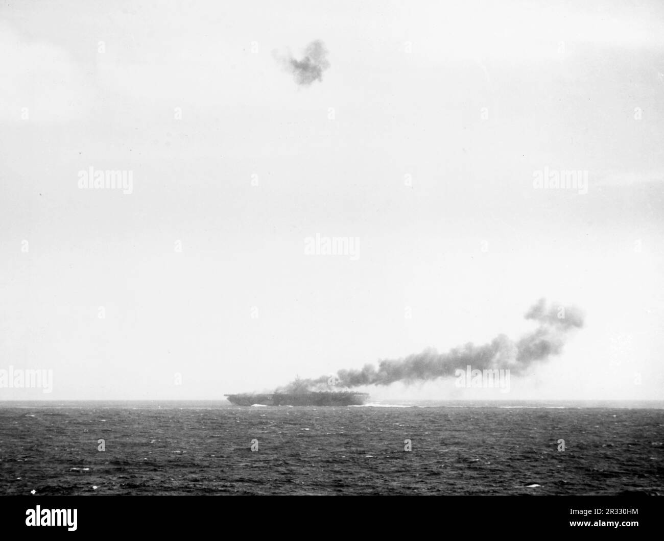 The U.S. Navy aircraft carrier USS Hancock (CV-19) burning as the result of a Japanese kamikaze attack on 25 November 1944. Antiaircraft fire had exploded the plane some 90 m above the ship, but a section of its fuselage landed amidships, and a part of the wing hit the flight deck and burst into flames. Prompt and skillful damage control quickly extinguished the blaze and prevented serious damage. Stock Photo