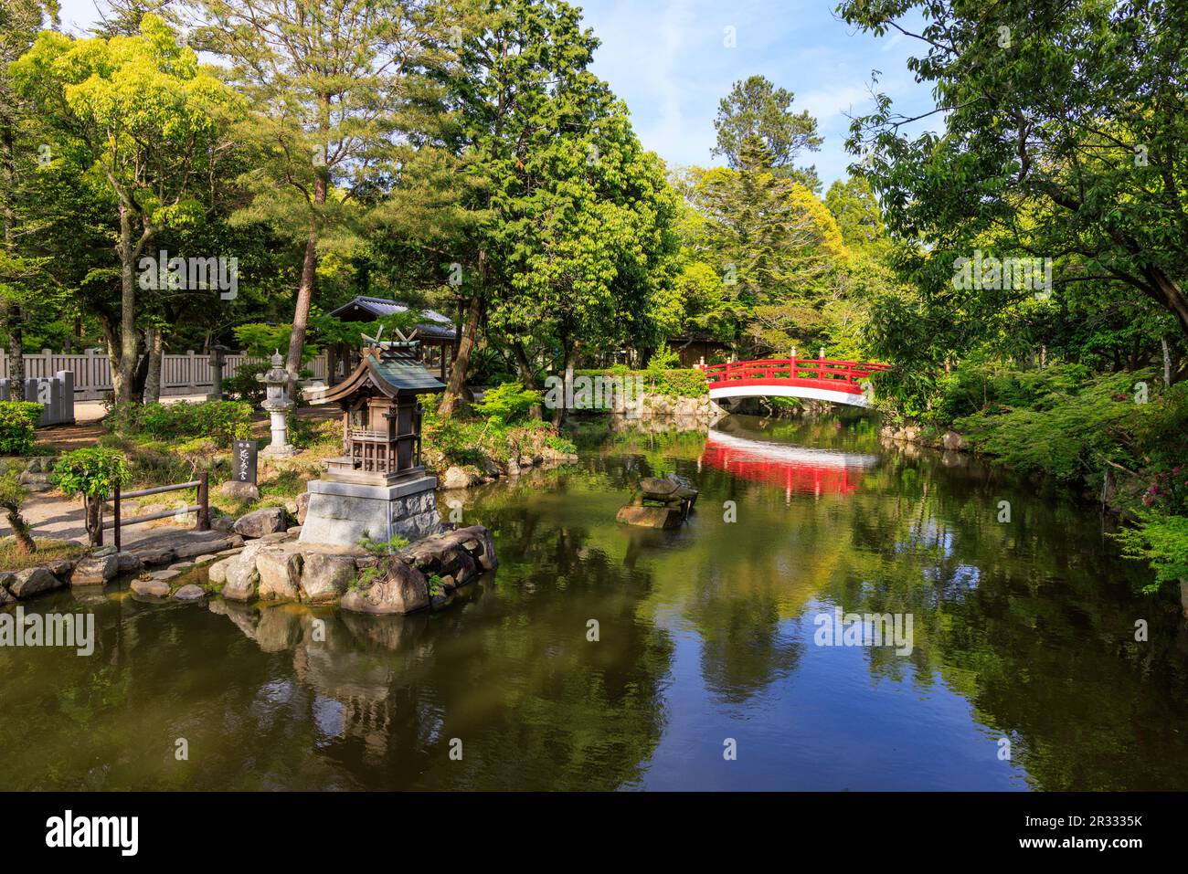 Red bridge reflects in calm pond in Japanese garden at shrine Stock Photo
