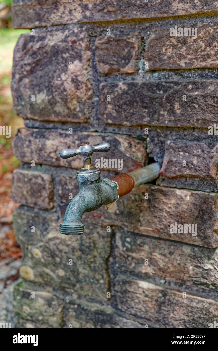 Metal water spigot with some rust and a turn on off handle sticking out of a stone wall closeup view Stock Photo