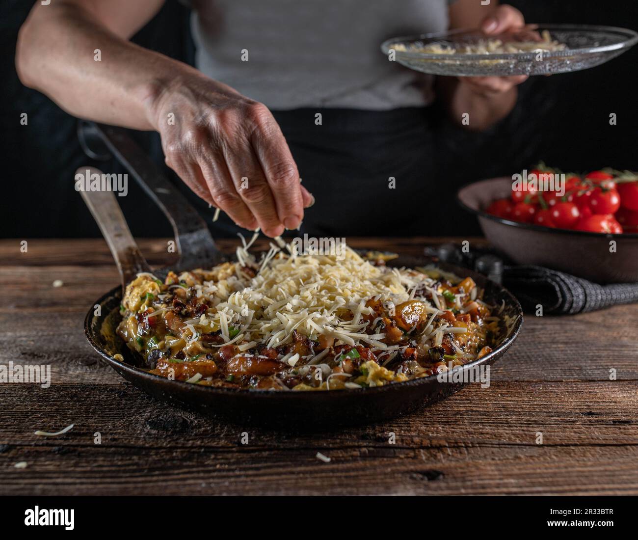 Woman sprinkles cheese over a pan with farmers breakfast. Stock Photo