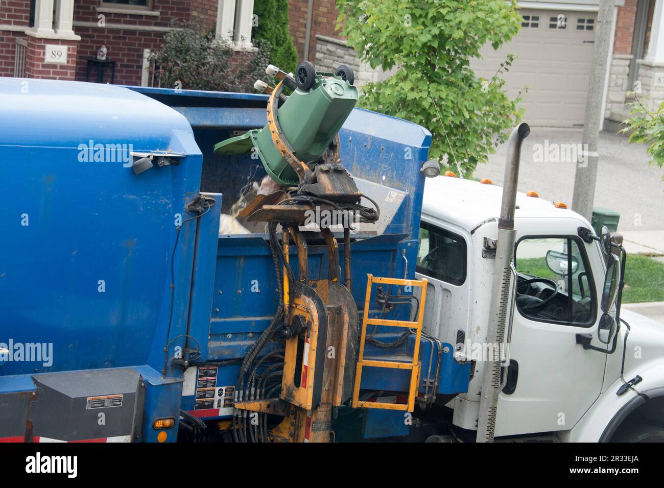 A mechanical hand lifts a standing rubbish bin and loads it into the desired section of the garbage truck Stock Photo