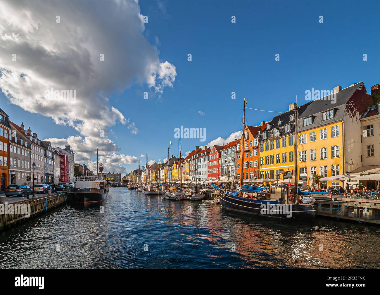 Copenhagen, Denmark - September 13, 2010: Line of iconic Nyhavn restaurant facades in bright colors plus other side canal under blue cloudscape. Boats Stock Photo