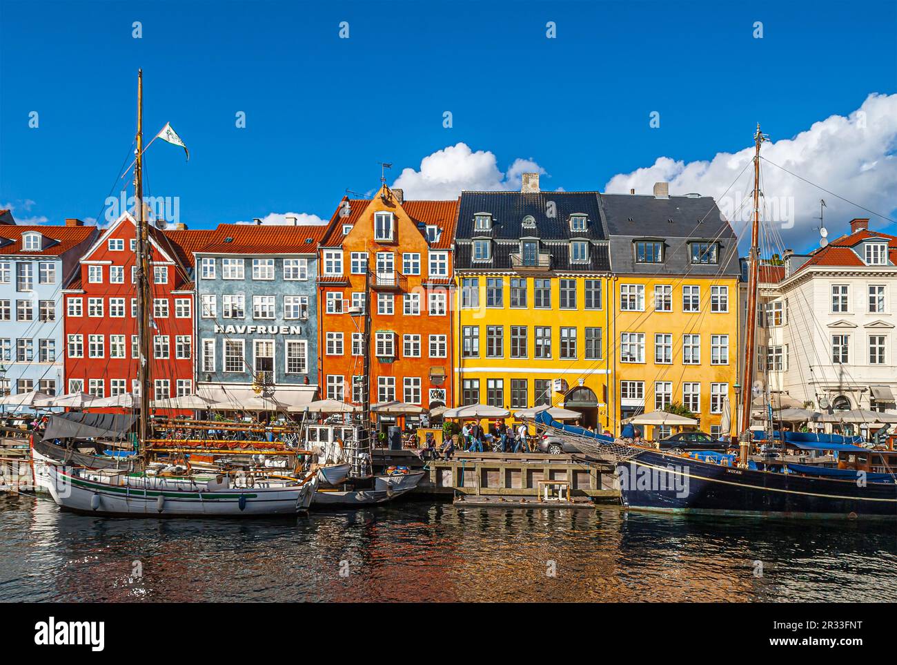 Copenhagen, Denmark - September 13, 2010: Line of iconic Nyhavn restaurant facades in bright colors at Nyhavnsbroen under blue cloudscape. Boats on wa Stock Photo