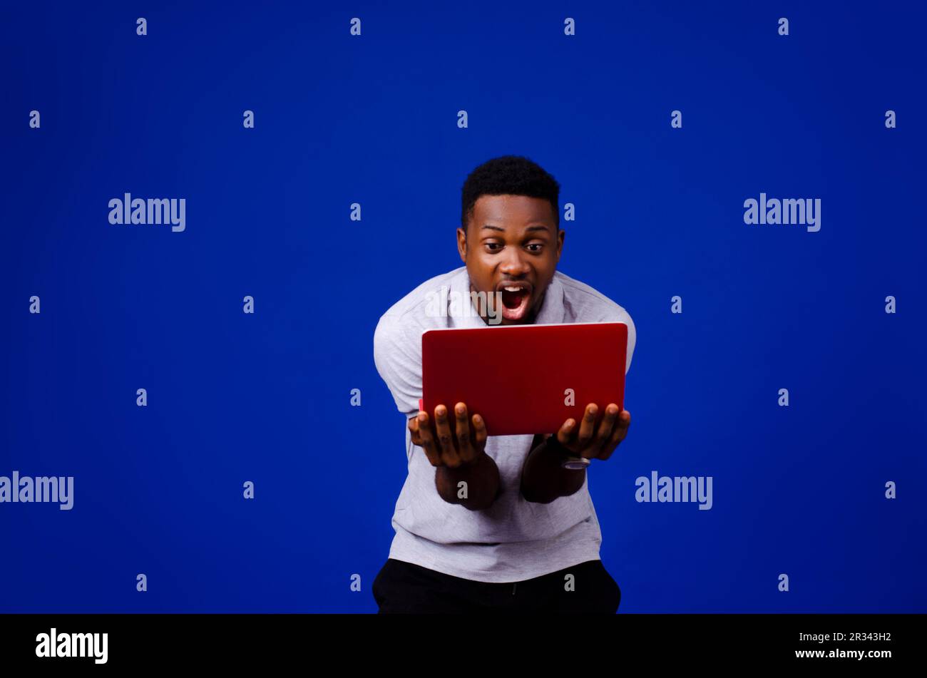 portrait of African man surprised with his mouth opened carrying a laptop isolated on a blue background Stock Photo