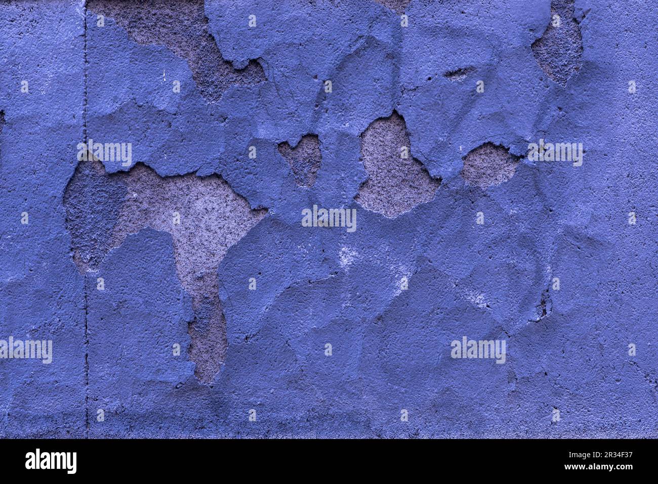 A surface of a concrete wall with huge chips in the blue plaster ...