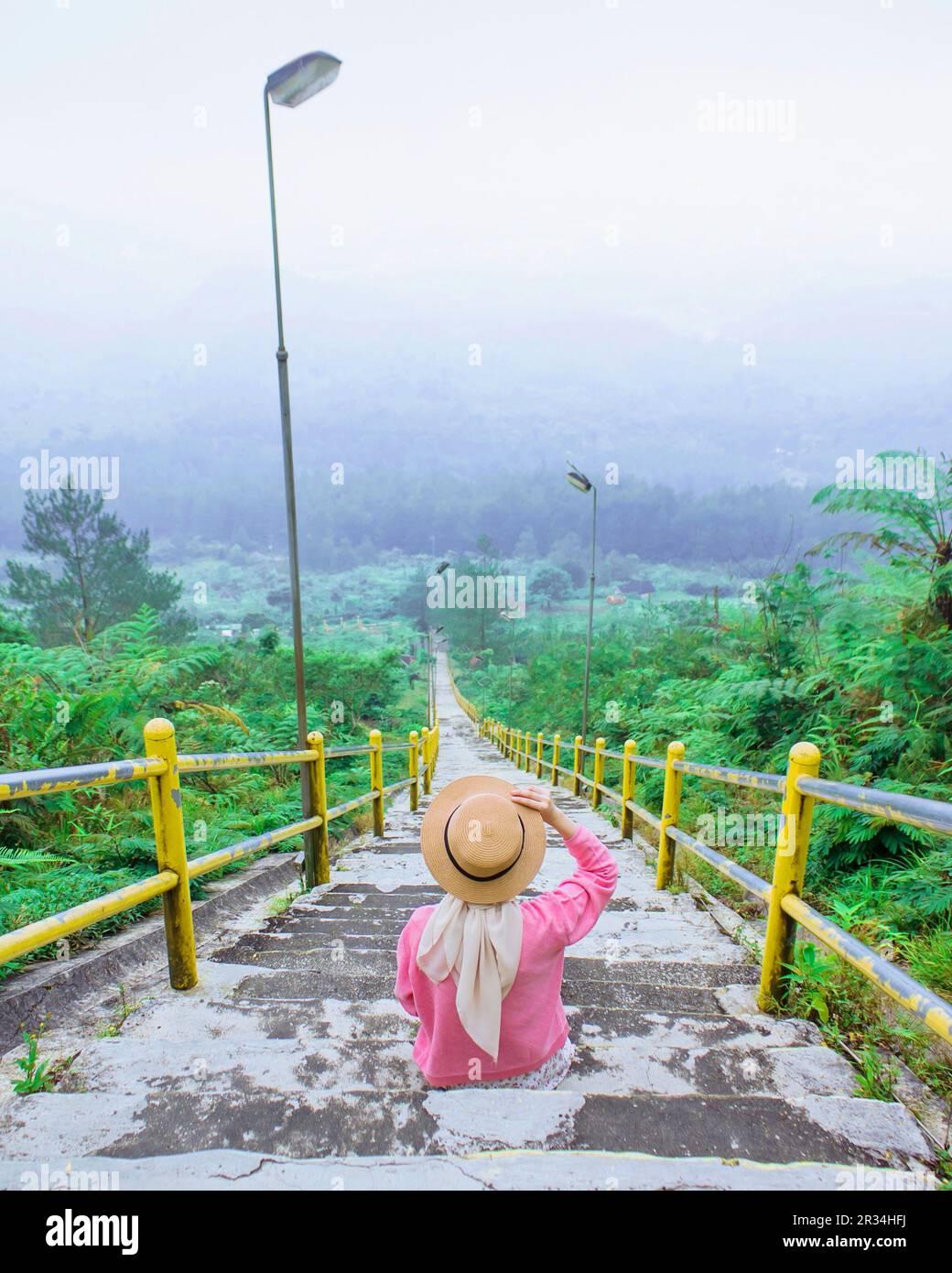 A female traveler sits on a ladder enjoying the natural beauty from above the mountains of Mount Galunggung, Tasikmalaya, West Java, Indonesia Stock Photo