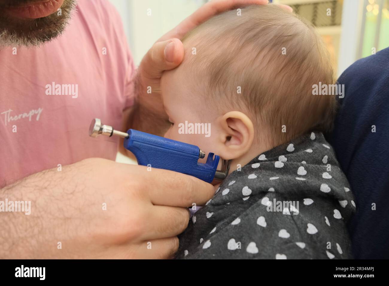 Little girl having ear piercing process with special piercing gun in