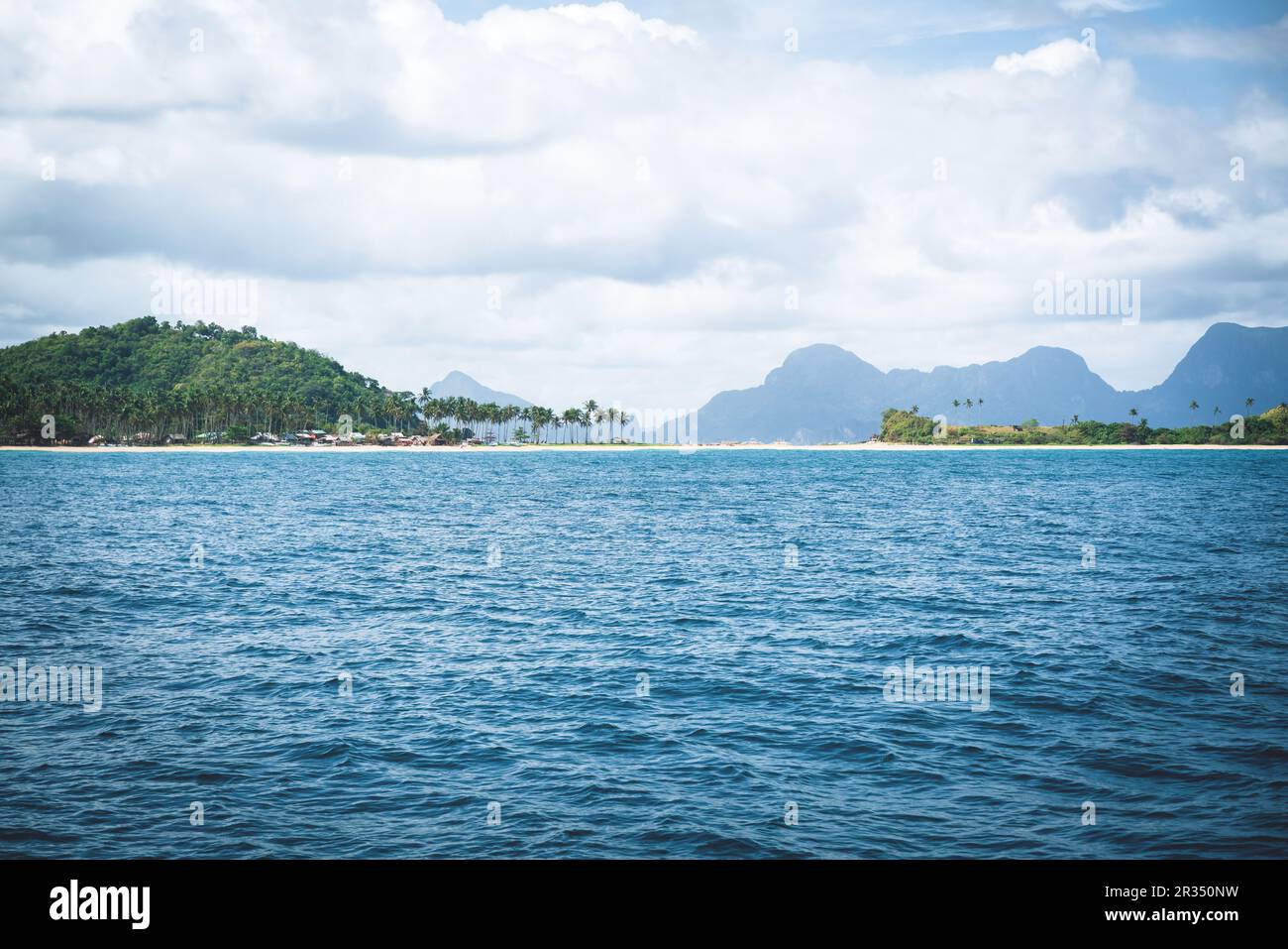 Blue ocean and village at white sand beach with palm trees along karst mountains of El Nido bay, Palawan, Philippines Stock Photo