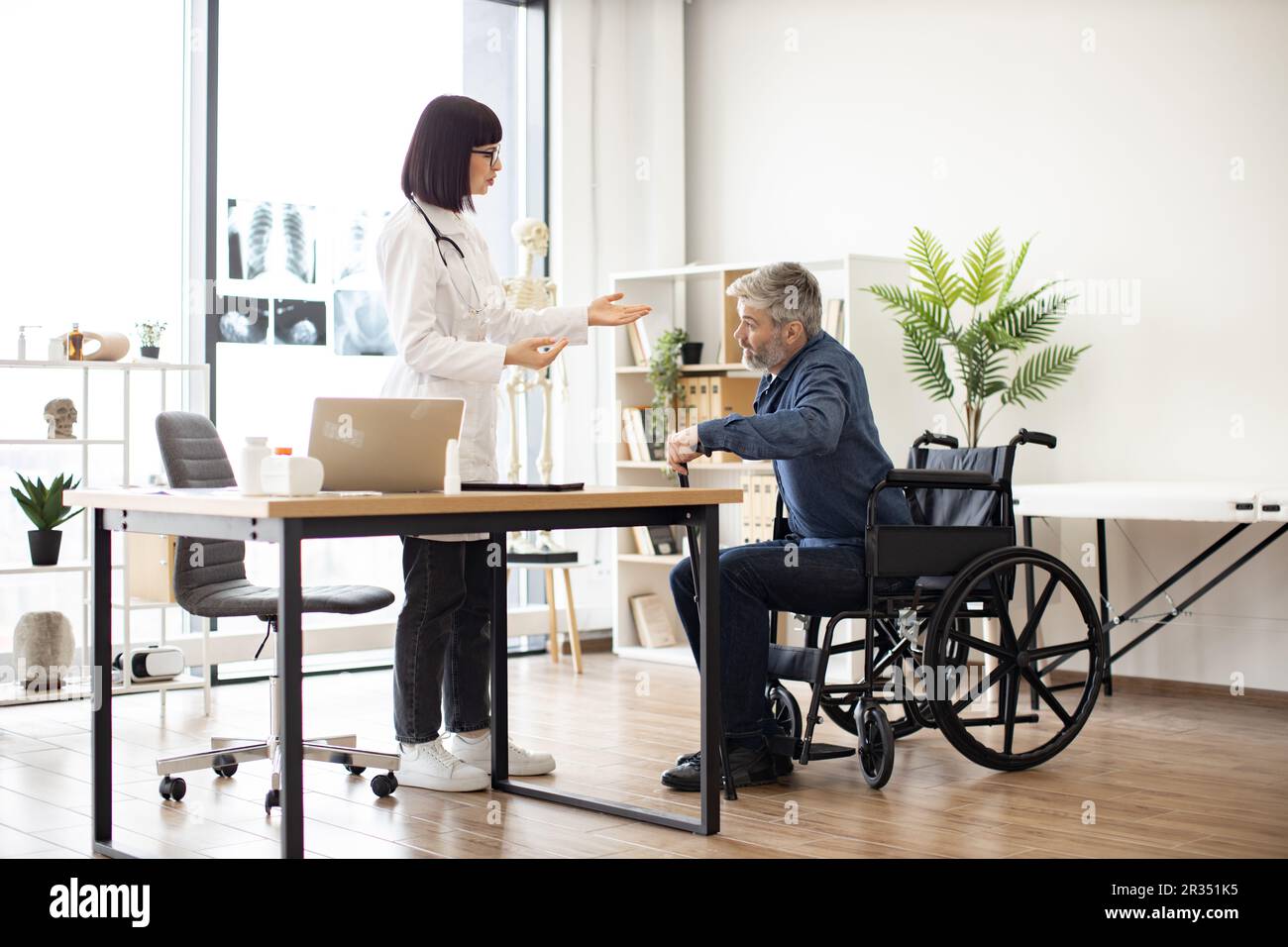 Young woman in lab coat helping mature man with walking cane to stand ...