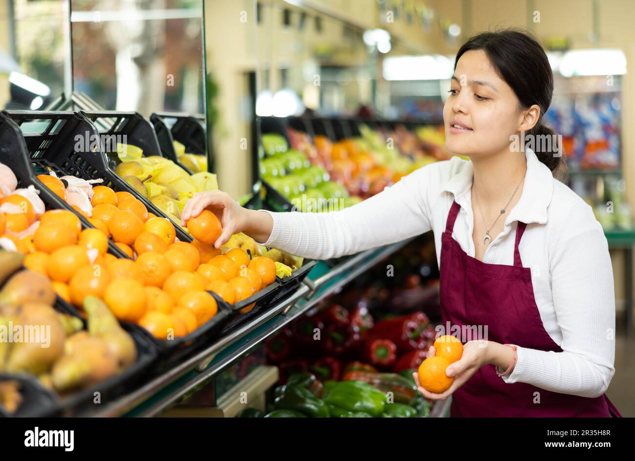 female-grocery-store-worker-lays-out-ripe-tangerines-on-counter-and