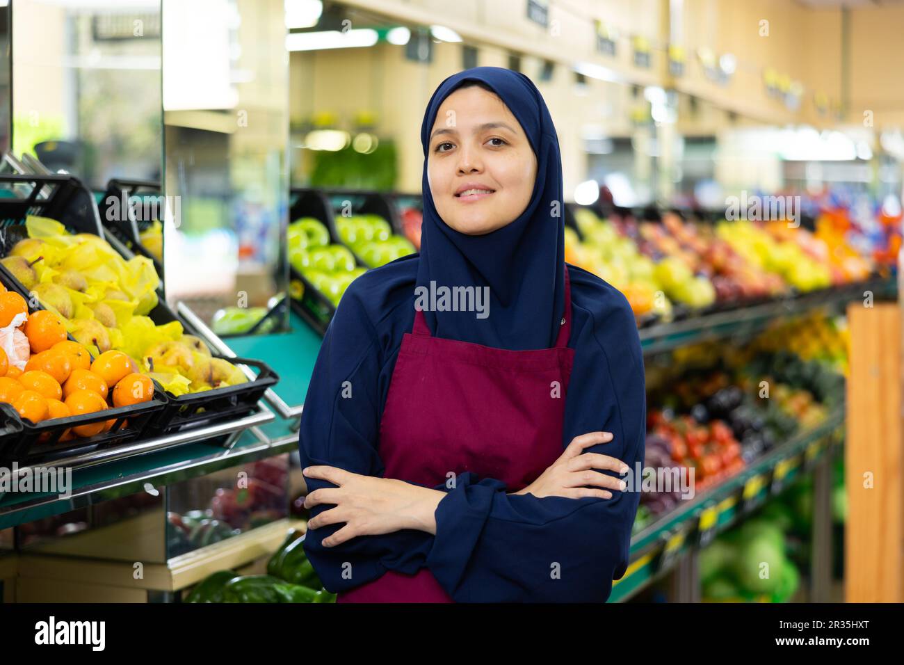 Portrait of friendly female salesperson in hijab and apron in grocery