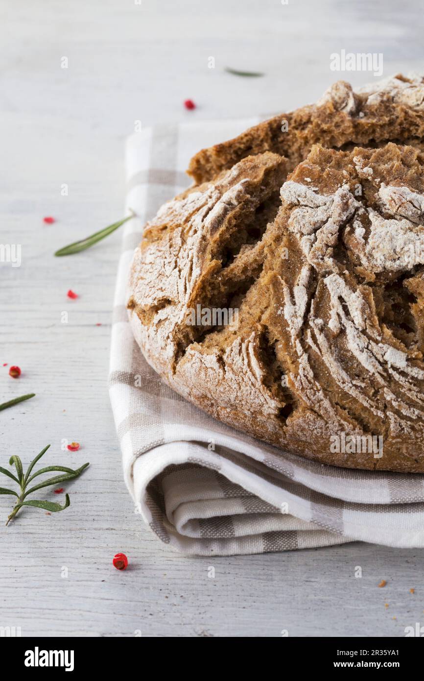 Country bread on a linen cloth with rosemary and pink peppercorns Stock Photo